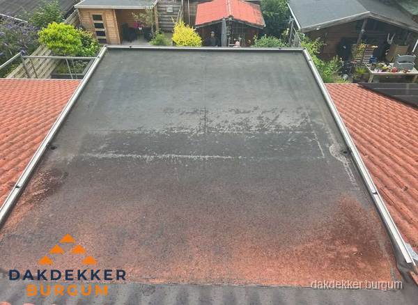 Verouderd plat dak met slijtage tussen schuine daken in Burgum Verouderd plat dak met slijtage tussen schuine daken in Burgum